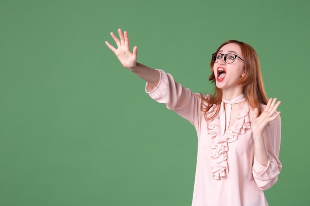 Vista frontal professora de blusa rosa olhando para cima em fundo verde biblioteca de trabalho escola mulher jovem trabalho lição livro cor estudante