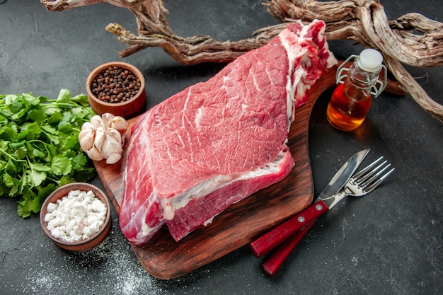 Vista frontal rebanada de carne cruda con condimentos y verduras sobre fondo oscuro color de cocción comida carne barbacoa comida carnicero