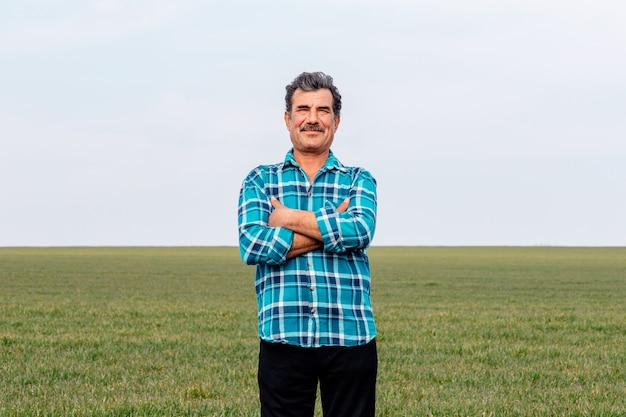 Una vista frontal de un retrato feliz propietario agricultor hombre con las manos cruzadas en el campo,