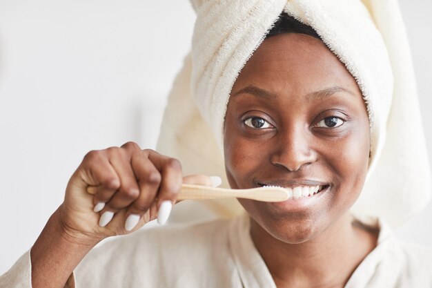 Vista frontal retrato de joven afroamericana cepillarse los dientes por la mañana y mirando a cámara, espacio de copia