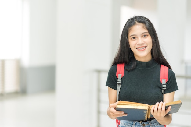 Vista frontal retrato de una joven estudiante universitaria alegre mujer adolescente asiática en relajado informal de regreso a la escuela llevar libros se encuentra en el edificio del campus