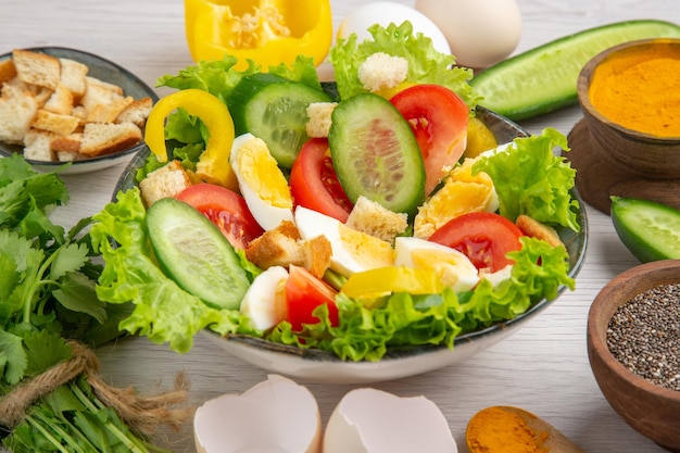 Vista frontal saborosa salada de legumes com ovos verdes e temperos em fundo branco refeição comida café da manhã cor madura