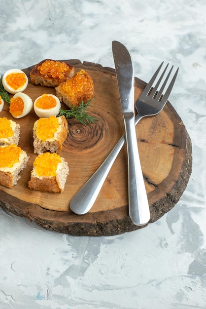 Vista frontal saborosos sanduíches de caviar com ovos cozidos e talheres na placa de madeira fundo branco comida café da manhã almoço peixe torrada refeição frutos do mar