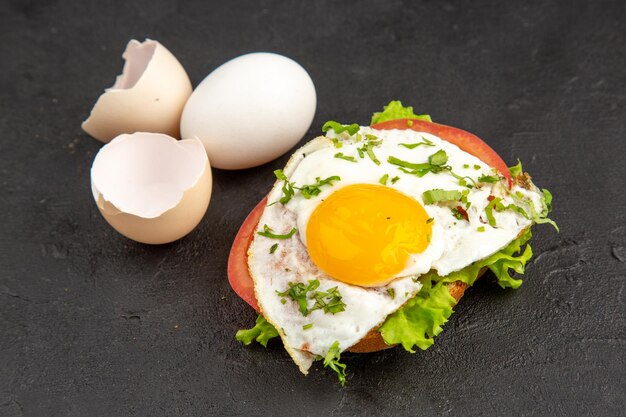 Vista frontal sabroso sándwich de huevo con huevos frescos sobre fondo gris oscuro hervir el desayuno tortilla pan de huevo almuerzo