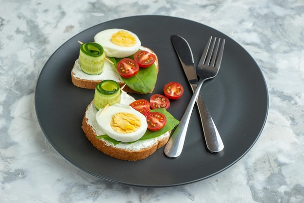 Vista frontal sabrosos sándwiches de huevo con cuchillo y tenedor placa interior superficie blanca sándwich dieta salud comida almuerzo pan hamburguesa tostada comida