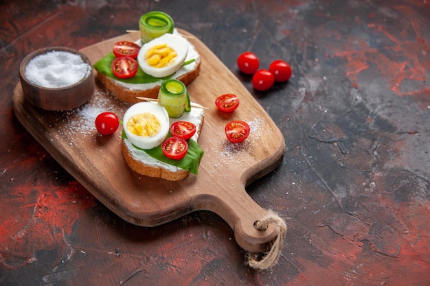 Vista frontal sabrosos sándwiches de huevo con tomates rojos en tabla de cortar fondo rojo oscuro almuerzo sándwich comida pan comida hamburguesa bocadillo tostada