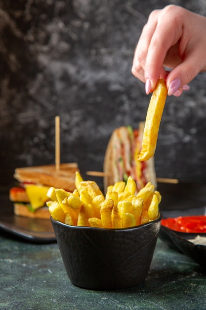 Foto vista frontal sabrosos sándwiches de jamón con papas fritas comiendo por la superficie oscura femenina