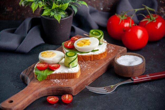 Vista frontal sanduíches saborosos com tomates pepinos e ovos na tábua de corte fundo escuro sanduíche hambúrguer comida lanche café da manhã torrada almoço