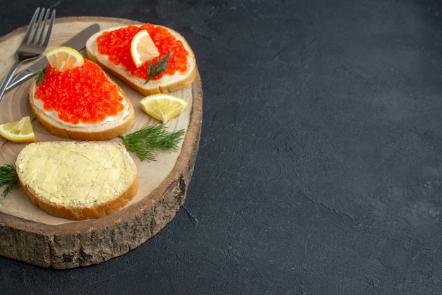 Vista frontal sándwiches de caviar con cubiertos en la superficie oscura de la tabla de cortar