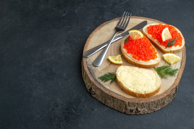 Vista frontal sándwiches de caviar con cubiertos en la superficie oscura de la tabla de cortar