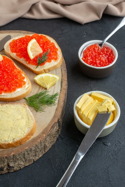 Vista frontal sándwiches de caviar con cubiertos en la superficie oscura de la tabla de cortar