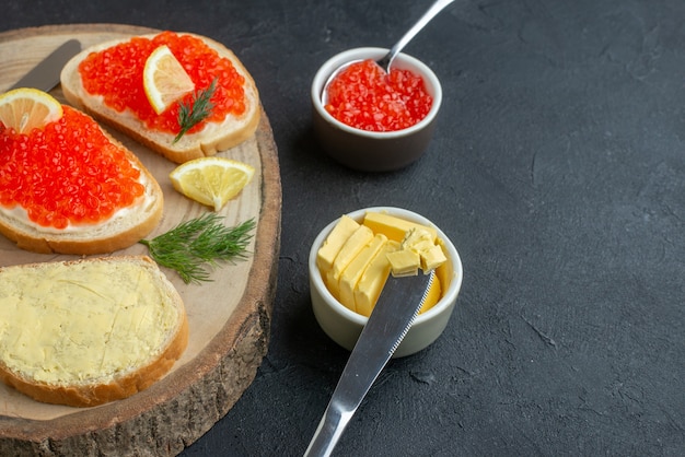 Vista frontal sándwiches de caviar con cubiertos en la superficie oscura de la tabla de cortar