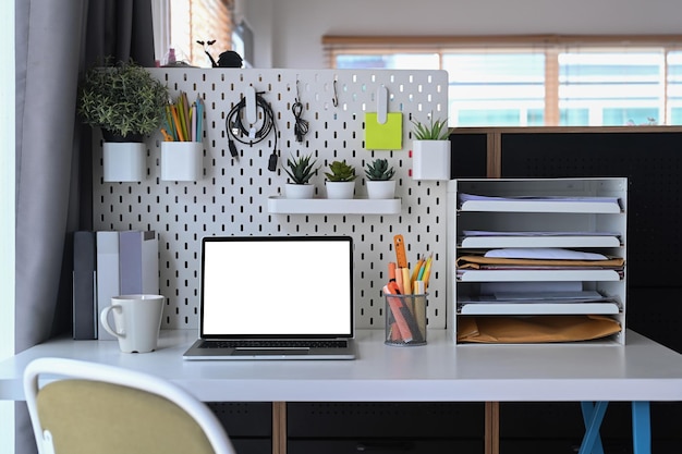 Vista frontal simula um computador portátil com tela em branco e suprimentos na mesa branca