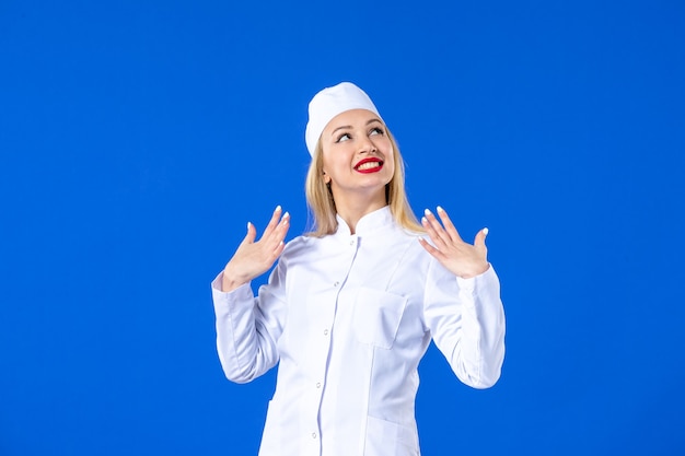 Vista frontal de la sonriente joven enfermera en traje médico sobre fondo azul enfermedad hospitalaria enfermedad covid medicina virus de drogas pandémicas salud