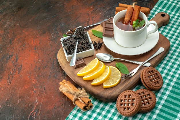 Vista frontal de una taza de té con galletas y limón sobre fondo oscuro color de la foto de la flor té de la galleta sabor a café