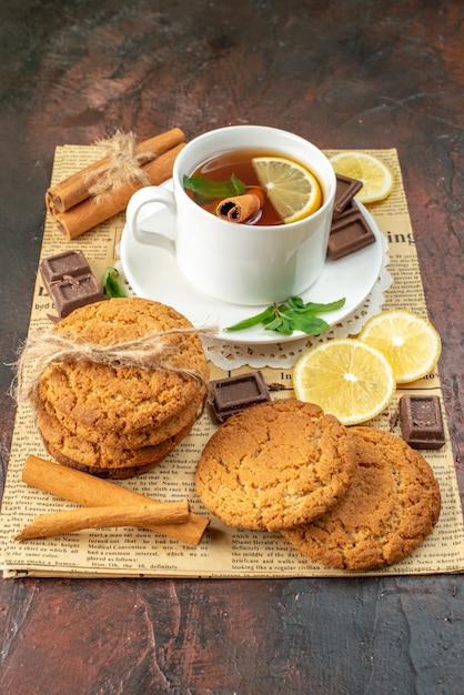 Vista frontal taza de té con limones amarillos frescos y galletas sobre fondo oscuro mañana color dulce ceremonia té desayuno frutas