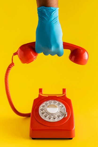 Foto vista frontal del teléfono retro con la mano en el guante sosteniendo el receptor