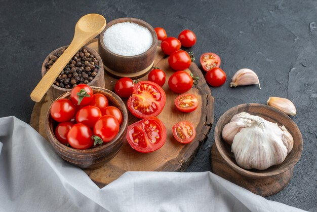 Vista frontal de tomates frescos y especias sobre tabla de madera toalla blanca ajos sobre superficie negra