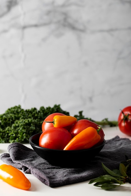 Vista frontal de tomates y pimientos en un recipiente con una toalla de cocina