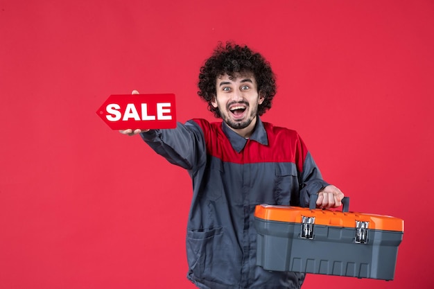 Vista frontal trabajador masculino con caja de herramientas y placa de venta sobre fondo rojo mecánico foto casa instrumento trabajador de trabajo de color