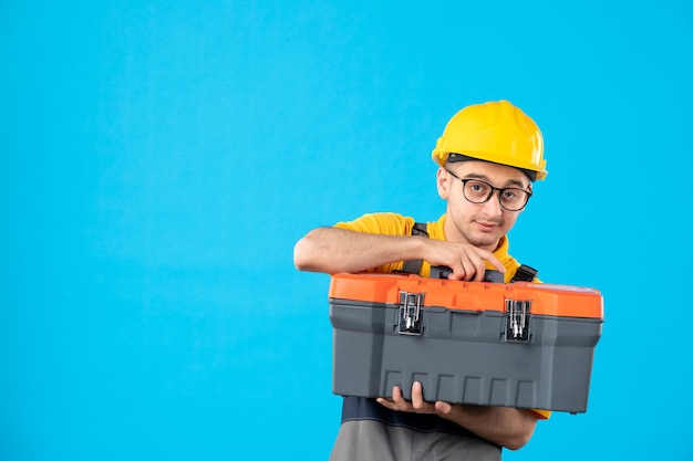 Foto vista frontal del trabajador de sexo masculino en uniforme y casco con caja de herramientas en sus manos en azul