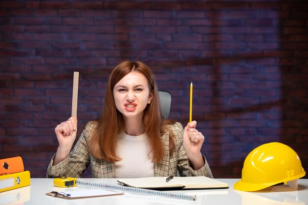 Vista frontal trabajadora en el sitio de construcción sentado detrás de la mesa agenda trabajo ingeniero gerente de plan de negocios corporativos