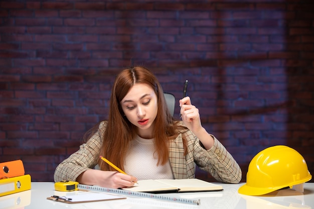 vista frontal trabalhadora no canteiro de obras sentada atrás da mesa agenda trabalho engenheira gerente de negócios corporativo trabalhando