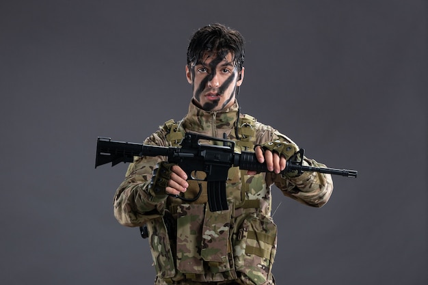 Vista frontal del valiente soldado luchando en camuflaje con ametralladora en pared gris