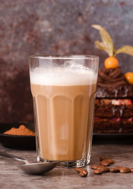 Vista frontal del vaso de chocolate con leche con cuchara y granos de café.