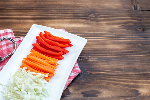Vista frontal de verduras en rodajas, zanahoria, pimientos y repollo sobre superficie marrón