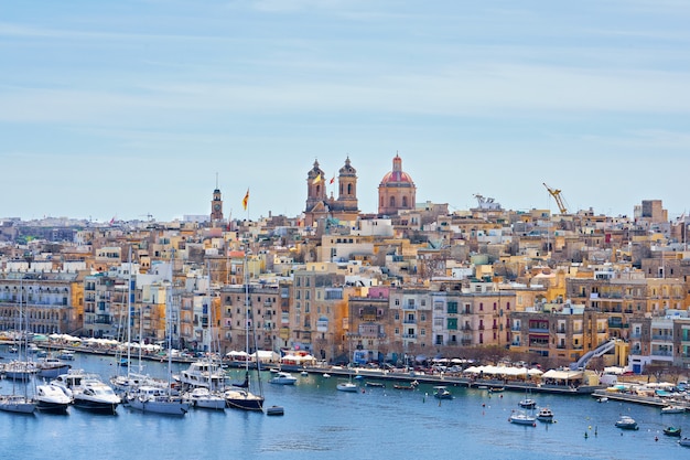 Vista geral na margem e na skyline da cidade de Birgu na baía com os barcos coloridos em Malta.