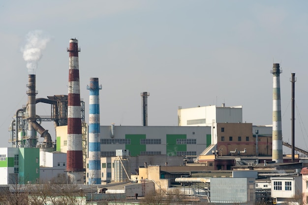 Una vista de una gran fábrica o empresa con grandes chimeneas humeantes contra un cielo azul Contaminación ambiental por desechos industriales Sale humo blanco de la chimenea