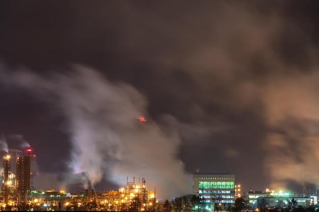 Vista de una gran fábrica o planta a la luz de la iluminación nocturna Sale mucho humo de las chimeneas de la fábrica Un accidente en una refinería de petróleo Un incendio en el territorio de la fábrica