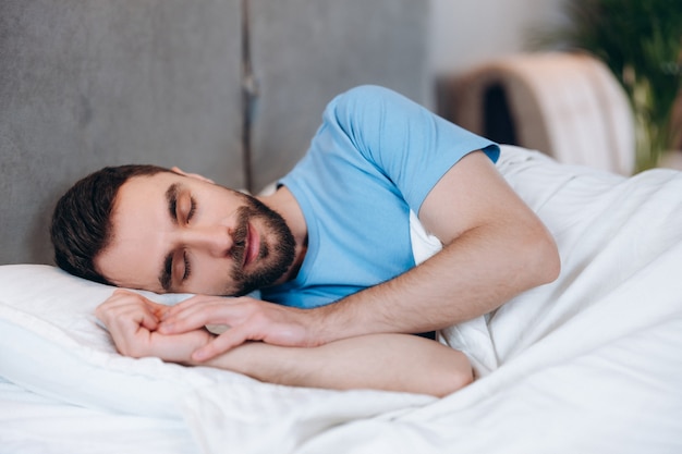 Vista del guapo hombre tranquilo con barba acostado sobre la almohada y durmiendo en la mañana