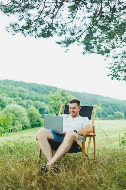 Vista de un hombre guapo acostado en una silla en la naturaleza y trabajando con una computadora portátil descansando solo mirando pensativo Un hombre en un viaje al campo el concepto del estilo de vida de la gente