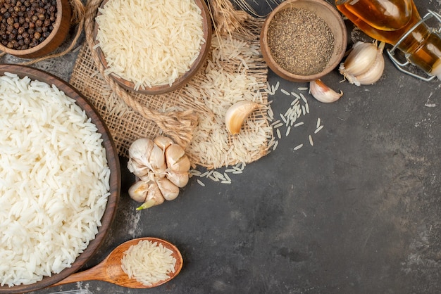 Vista HORIZONTAL de tigelas marrons de arroz longo perfeitas em toalha de cor nua garrafa de óleo caída pimentas na mesa escura