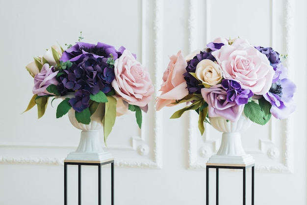 Vista horizontal de hermosas flores artificiales en colores rosa y púrpura en jarrones blancos sobre soportes en el salón para la ceremonia de boda Decoración floral