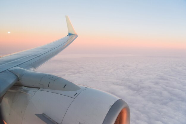 La vista desde el iluminador del avión hasta el ala, la turbina del avión y las nubes esponjosas al amanecer. Volando sobre las nubes