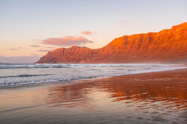 Vista de la increíble playa durante la puesta de sol roja Agua del océano y montañas de la costa en el fondo con cielo despejado Vacaciones de verano y hermoso destino escénico