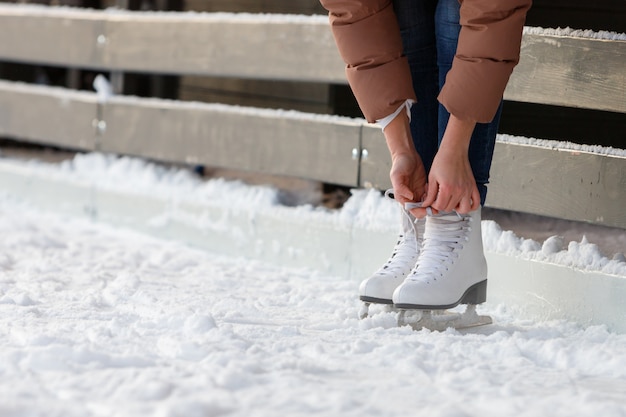 Vista inferior de cordones de zapatos femeninos / usar patines blancos en la pista de hielo en día de invierno. Fines de semana actividades al aire libre en climas fríos