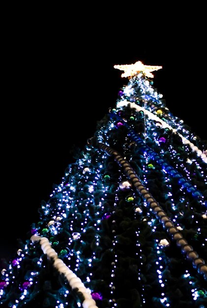 Foto vista inferior da árvore de natal alta decorada com luzes, guirlandas, estrela no fundo preto