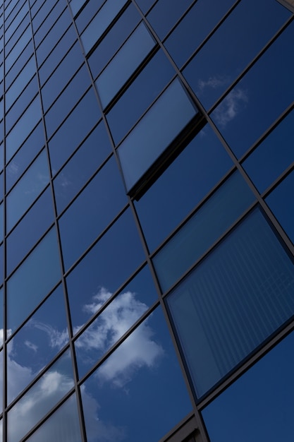 Vista inferior da superfície de vidro azul da parede do edifício refletindo o céu azul com nuvens