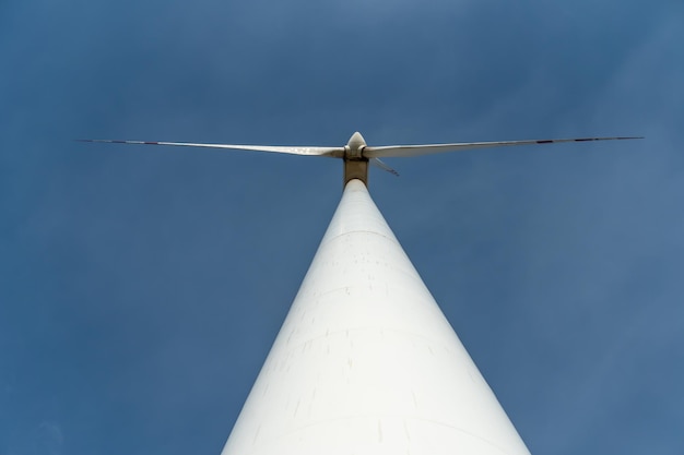 Vista inferior de um moinho de vento moderno contra um céu azul As lâminas brancas da turbina eólica Tubo de produção de energia limpa e renovável e moinho de vento base de apoio close-up