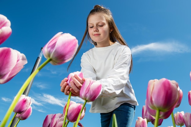 Vista inferior de uma garota olhando para uma flor de tulipa com fundo do céu