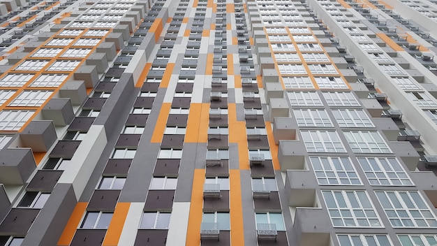 Vista inferior de la fachada de un nuevo edificio residencial de varios pisos con balcones y ventanas grises y naranjas.