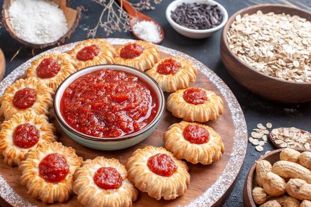 Vista inferior galletas con mermelada y mermelada tazón sobre tabla de madera avena en tazón nueces en tazones sobre fondo oscuro