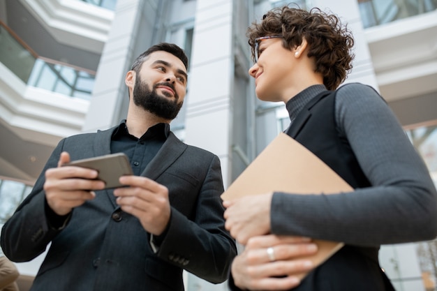 Vista inferior de jóvenes socios comerciales ambiciosos en ropa formal discutiendo el proyecto con smartphone en la oficina