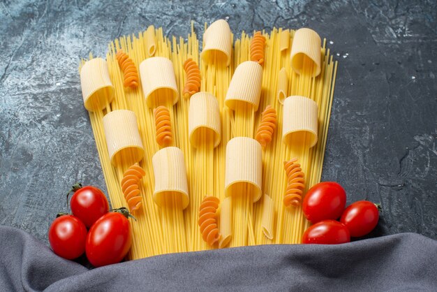 vista inferior massas crus rigatoni espaguete espirais tomate cereja xale roxo na mesa cinza