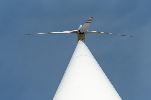 Vista inferior de un molino de viento moderno contra un cielo azul Las palas blancas de la turbina eólica La tubería de producción de energía limpia y renovable y el molino de viento base de apoyo se cierran