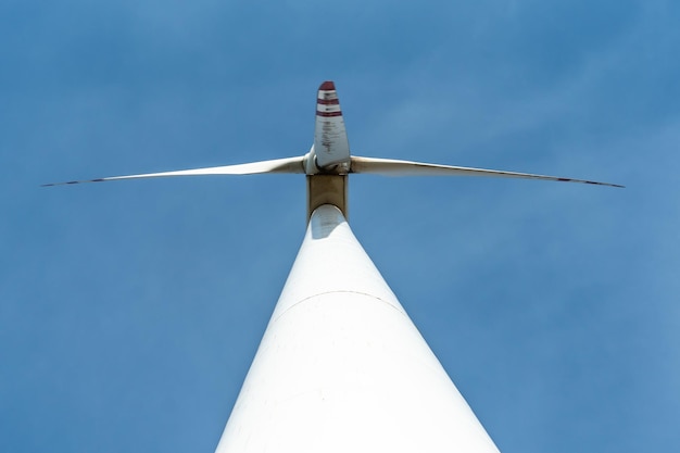 Vista inferior de un molino de viento moderno contra un cielo azul Las palas blancas de la turbina eólica La tubería de producción de energía limpia y renovable y el molino de viento base de apoyo se cierran